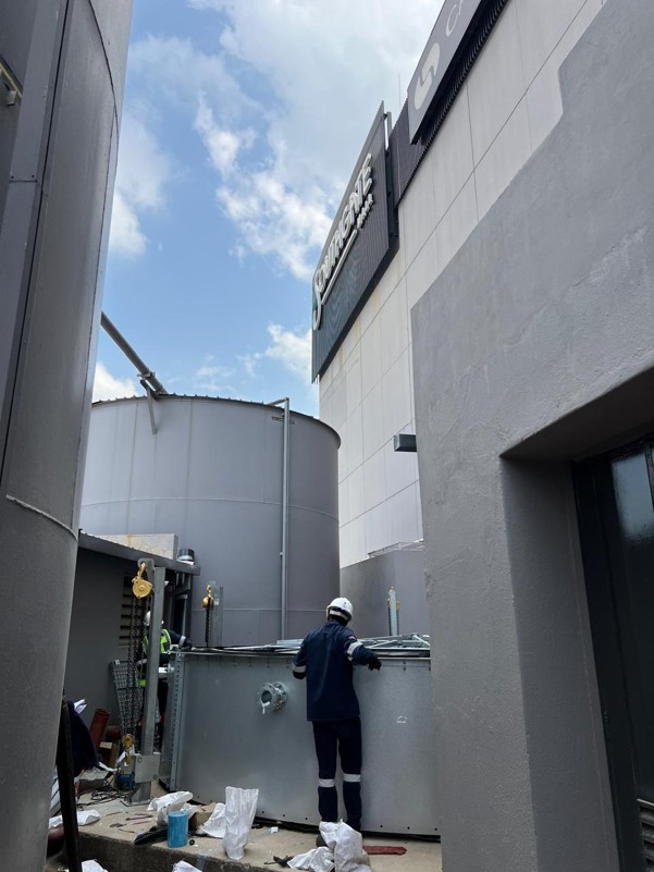 Videx cylindrical Aluzinc fire-water tank being installed in the highly restricted services area at Southgate Mall, positioned between existing buildings.